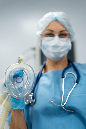 A healthcare professional in a blue scrub suit is holding a mask, poised for intubation in a clinical setting.