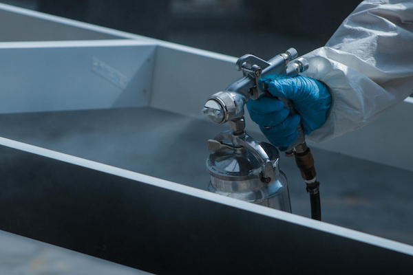 A person in a white coat applies an industrial hydrophilic coating to a metal surface using a spray technique.